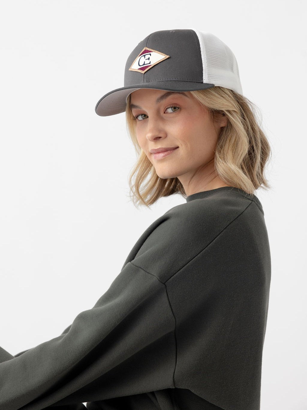 Woman looking at camera wearing charcoal/white diamond mesh trucker hat |Color:Charcoal/White