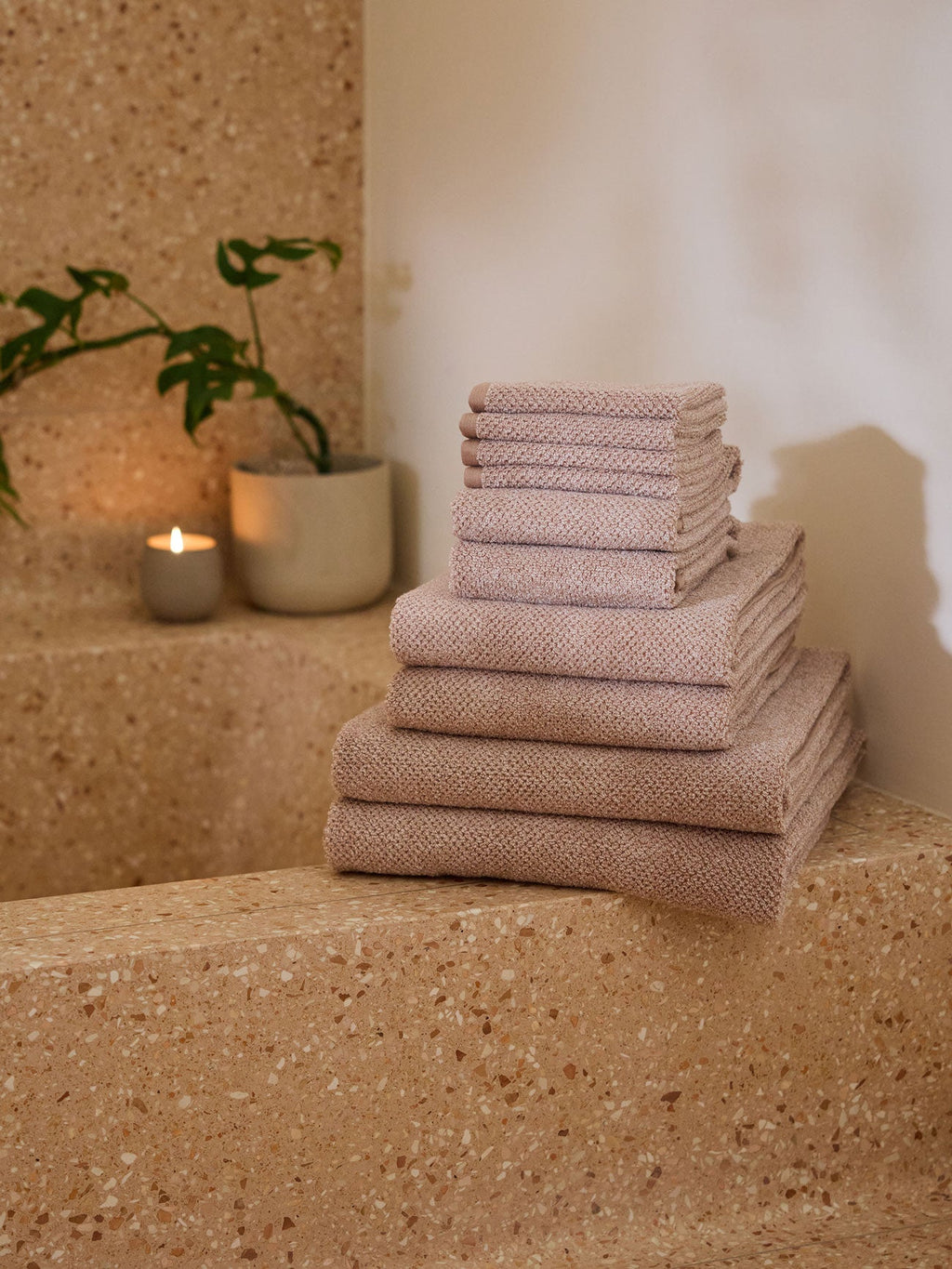 A pair of Nantucket Bath Towels in Heathered Clay are stacked on the edge of a stone tub. A plant and lit candle are in the background. |Color:Heathered Clay