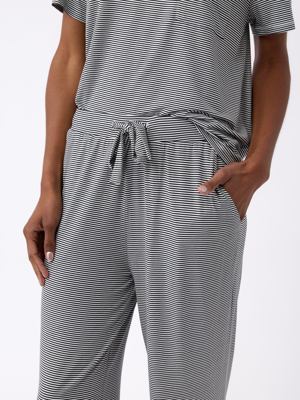 A person is wearing a gray and white striped, short-sleeve shirt with a tied waist, paired with Cozy Earth's Women's Bamboo Stretch-Knit Pant. Their hands are in their pockets against a plain white background. |Color:Eclipse Mini Stripe