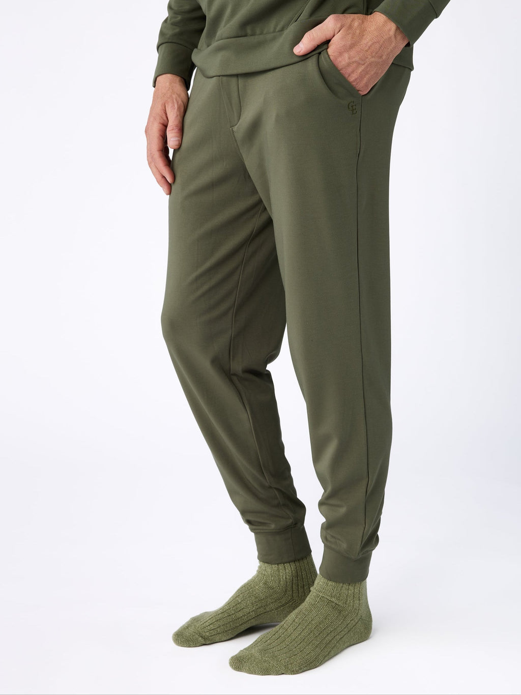 A person dressed completely in Cozy Earth's Men's Ultra-Soft Bamboo Pullover Crew in green stands against a white background. They have their hands in the pockets of their olive green pants and are wearing matching green socks. |Color:Olive