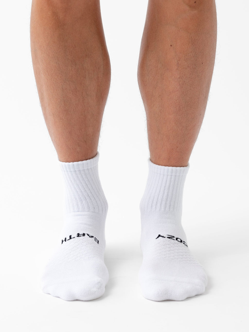 A person wearing Cozy Earth's Essential Quarter Sock 6-Pack stands on a white surface, showing only their lower legs and feet. |Color:White