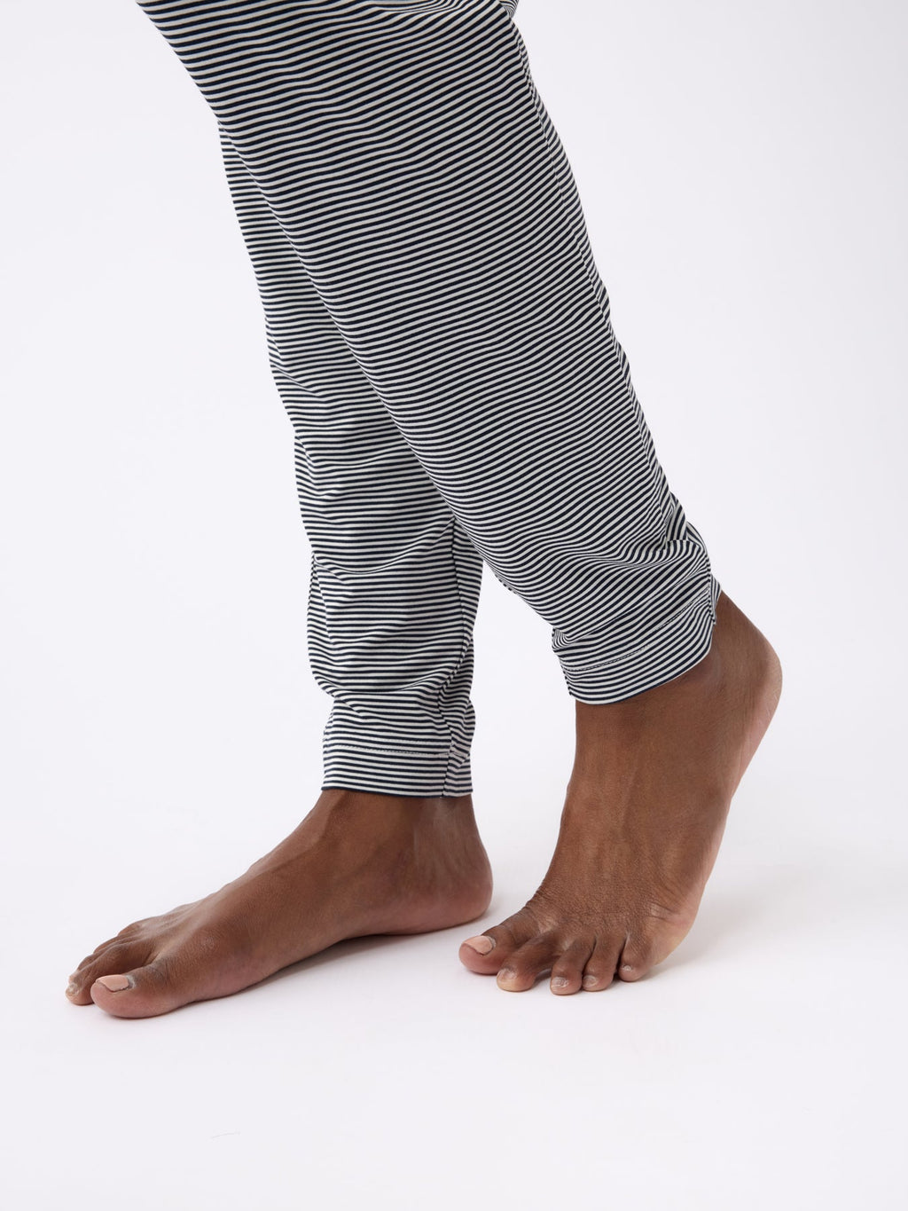 Bare feet step forward in Cozy Earth's Women's Bamboo Stretch-Knit Tapered Pant, featuring black and white stripes with rolled-up cuffs, set against a plain white background. |Color:Eclipse Mini Stripe