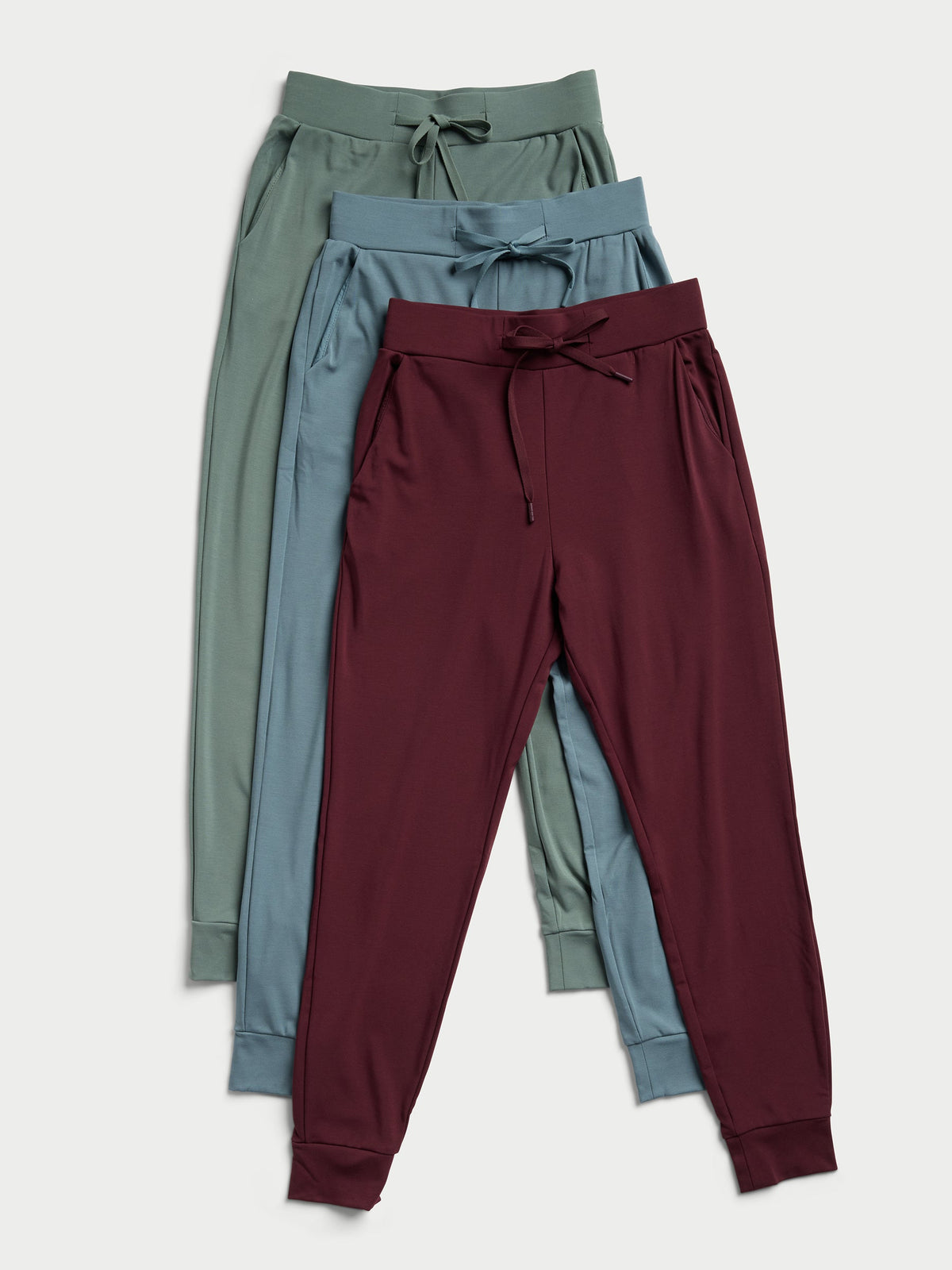 Three pairs of Cozy Earth's Women's Bamboo Jogger Pants TALL in olive green, teal, and maroon are stacked on top of each other. Each pair is designed with an elastic waistband, a drawstring, and cuffed ankles. They are showcased against a light background. |Color:Oakmoss