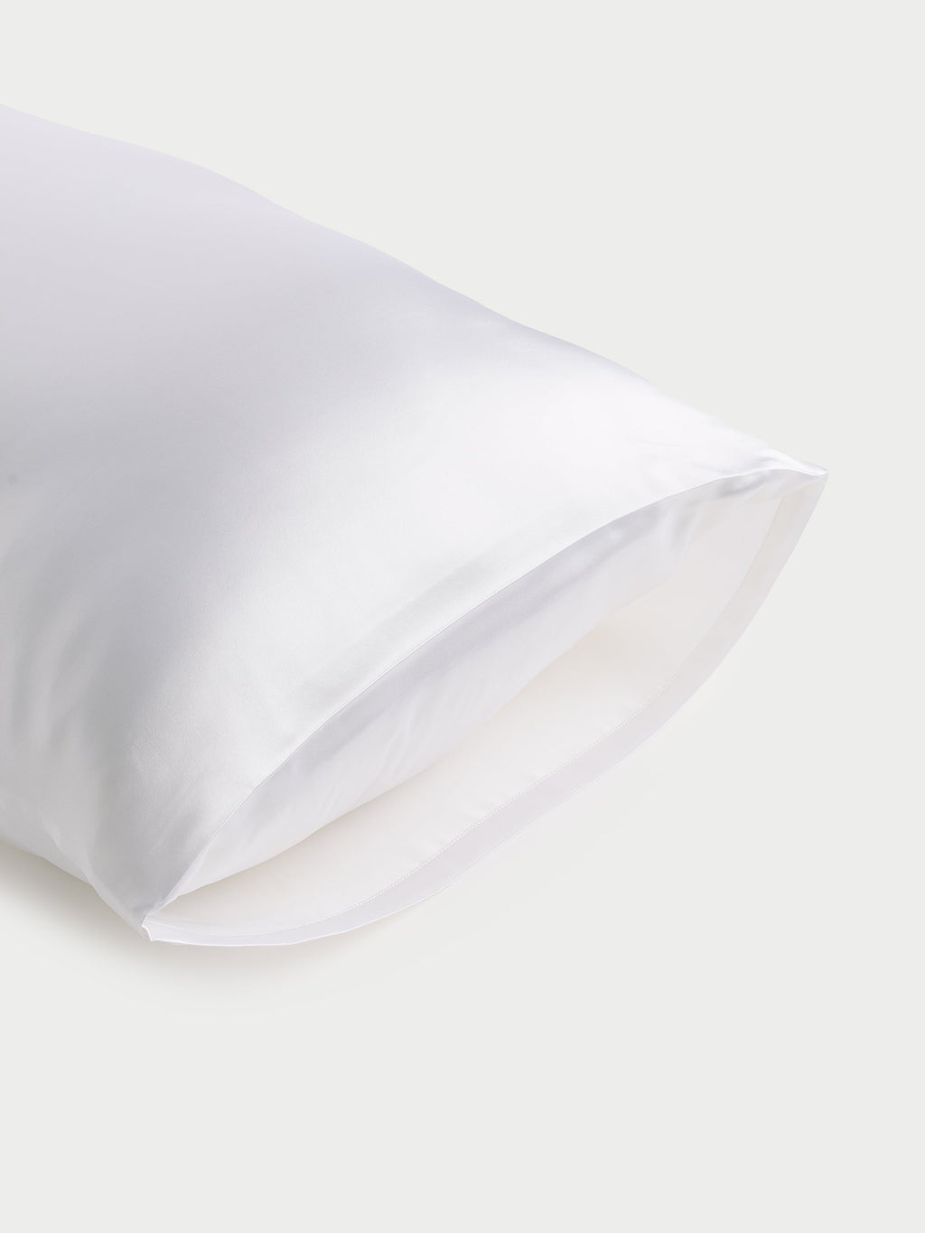 The Cozy Earth Silk Pillowcase, with its smooth and glossy texture, is showcased against a light gray background. The fabric drapes softly, accentuating its luxurious and sleek appearance. |Color:White