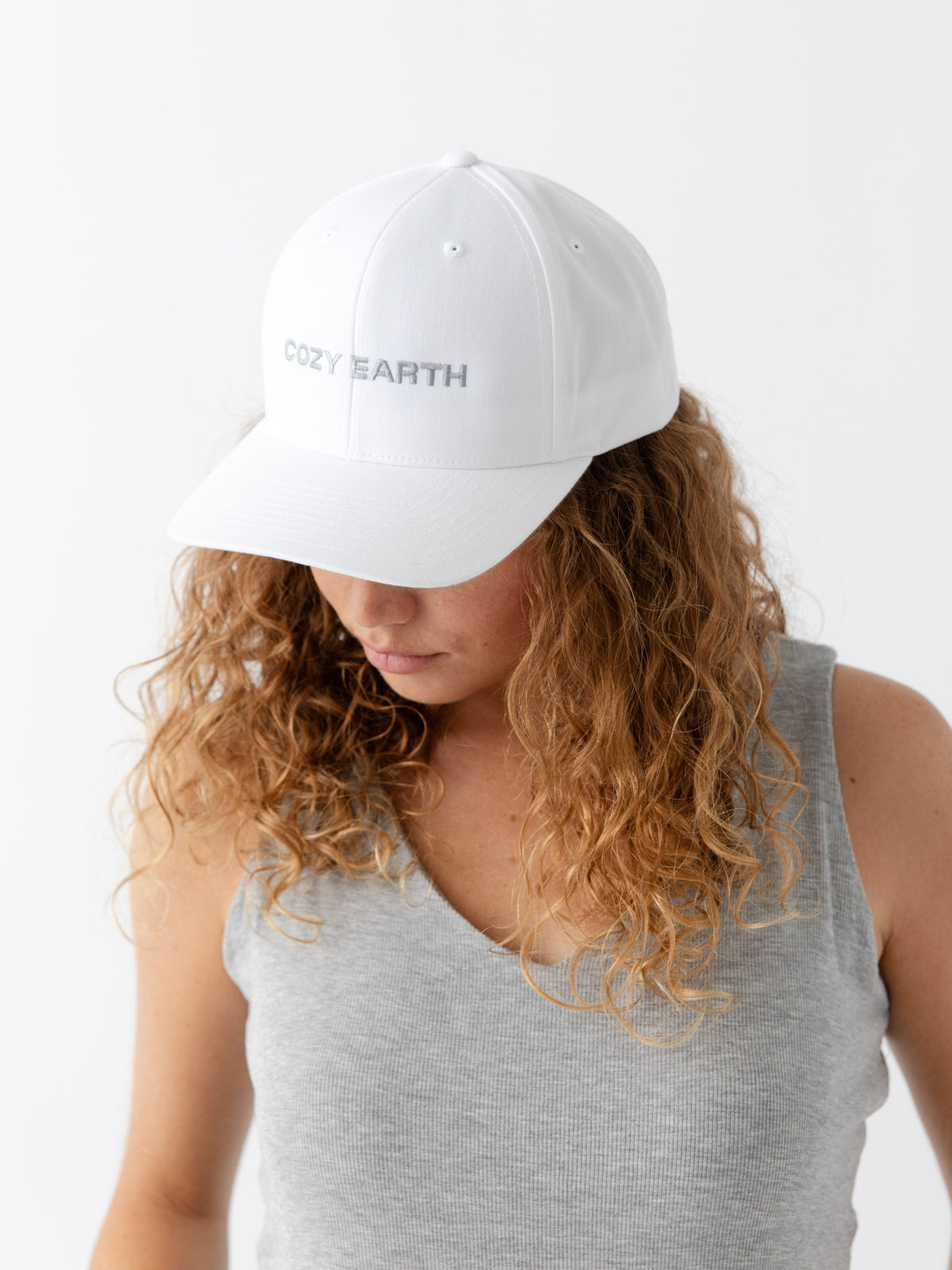 A woman wearing a White cap with 'COZY EARTH' text on a white background |Color:White/Stone