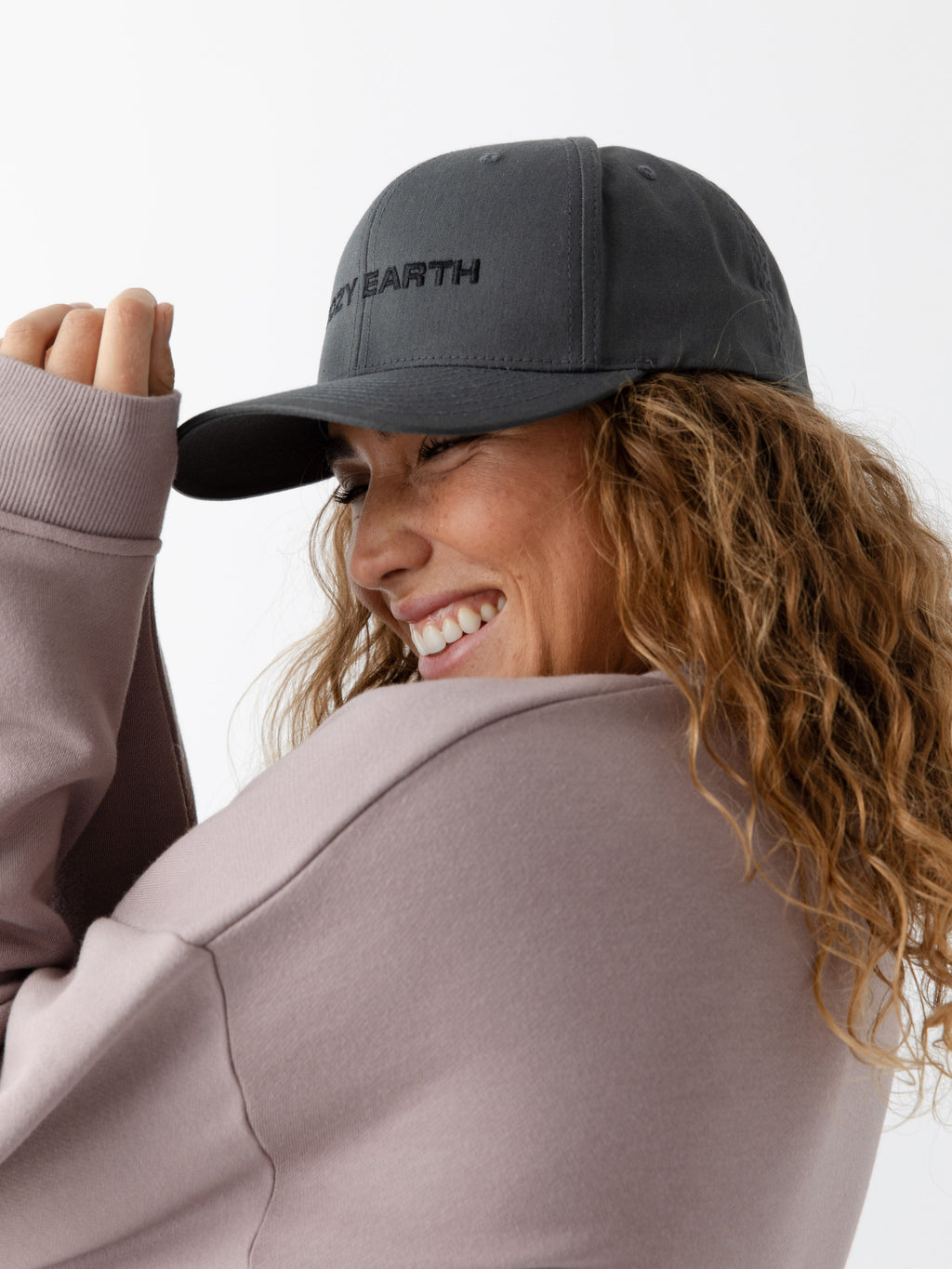 A woman wearing a grey cap with 'COZY EARTH' text on a white background |Color:Charcoal/Black