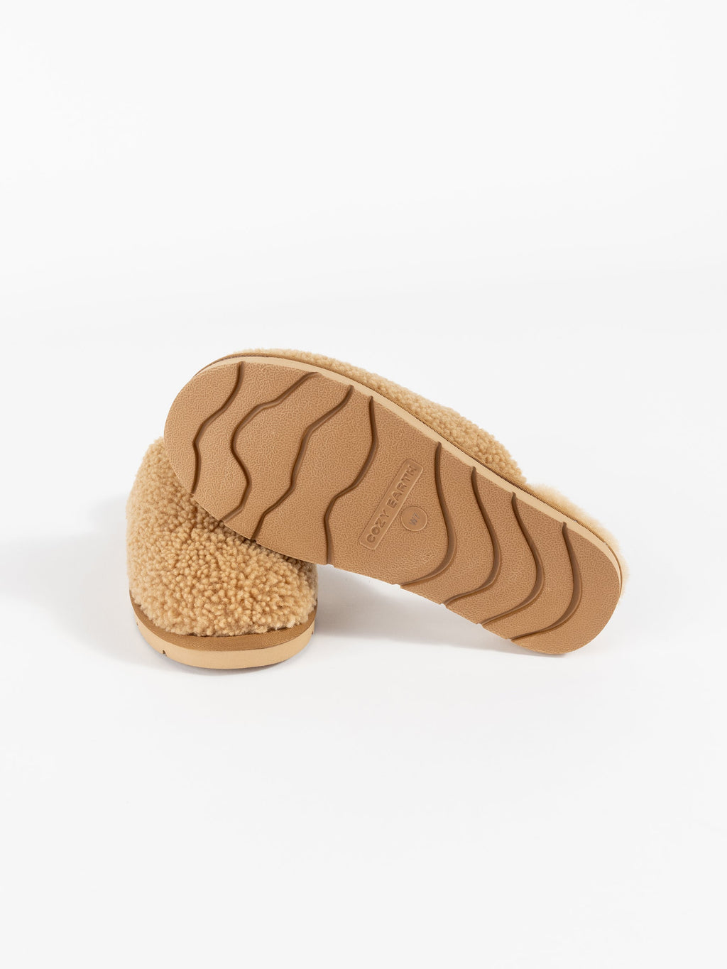 A pair of Cozy Earth's Puffy Sheep Slippers, featuring a tan fleece texture and embossed rubber soles with a wavy grip pattern, displayed in a studio setting. The slippers are arranged to showcase both the top and bottom views. |Color:Fawn