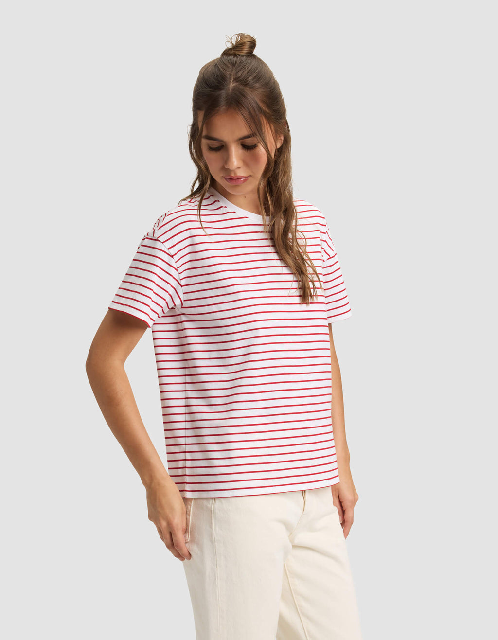 A woman models the Cozy Earth Women's All Day Tee—a white T-shirt with red and blue stripes—paired with off-white pants, standing against a light gray background. |Color:Crimson Stripe