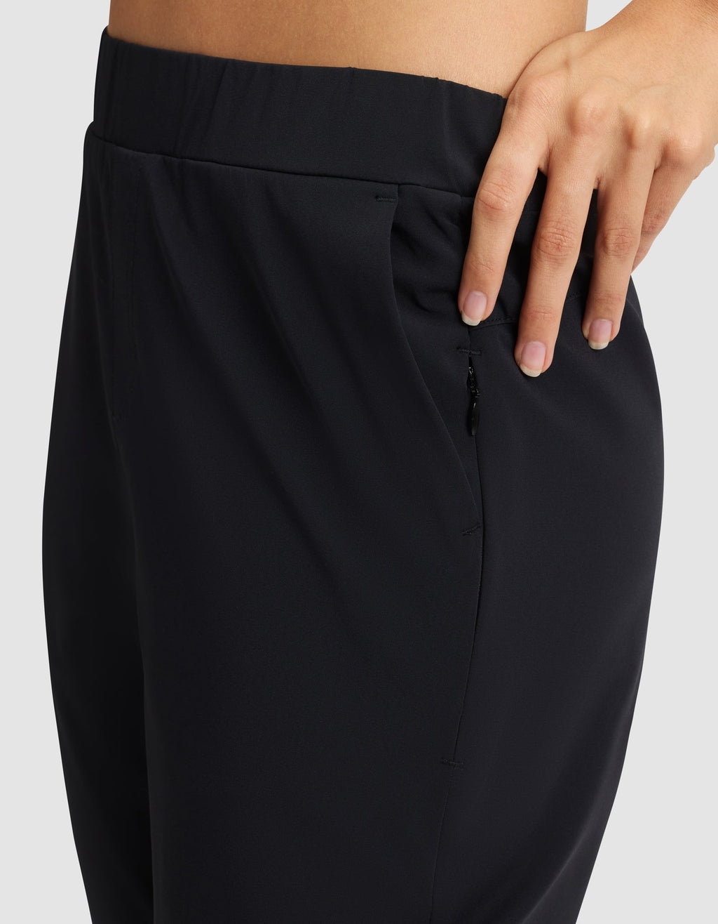 A close-up of a person wearing Cozy Earth's Women's Always Cropped Pant in black, featuring a zipper pocket and their hand resting on the waistband against a plain, light-colored background. |Color:Jet Black