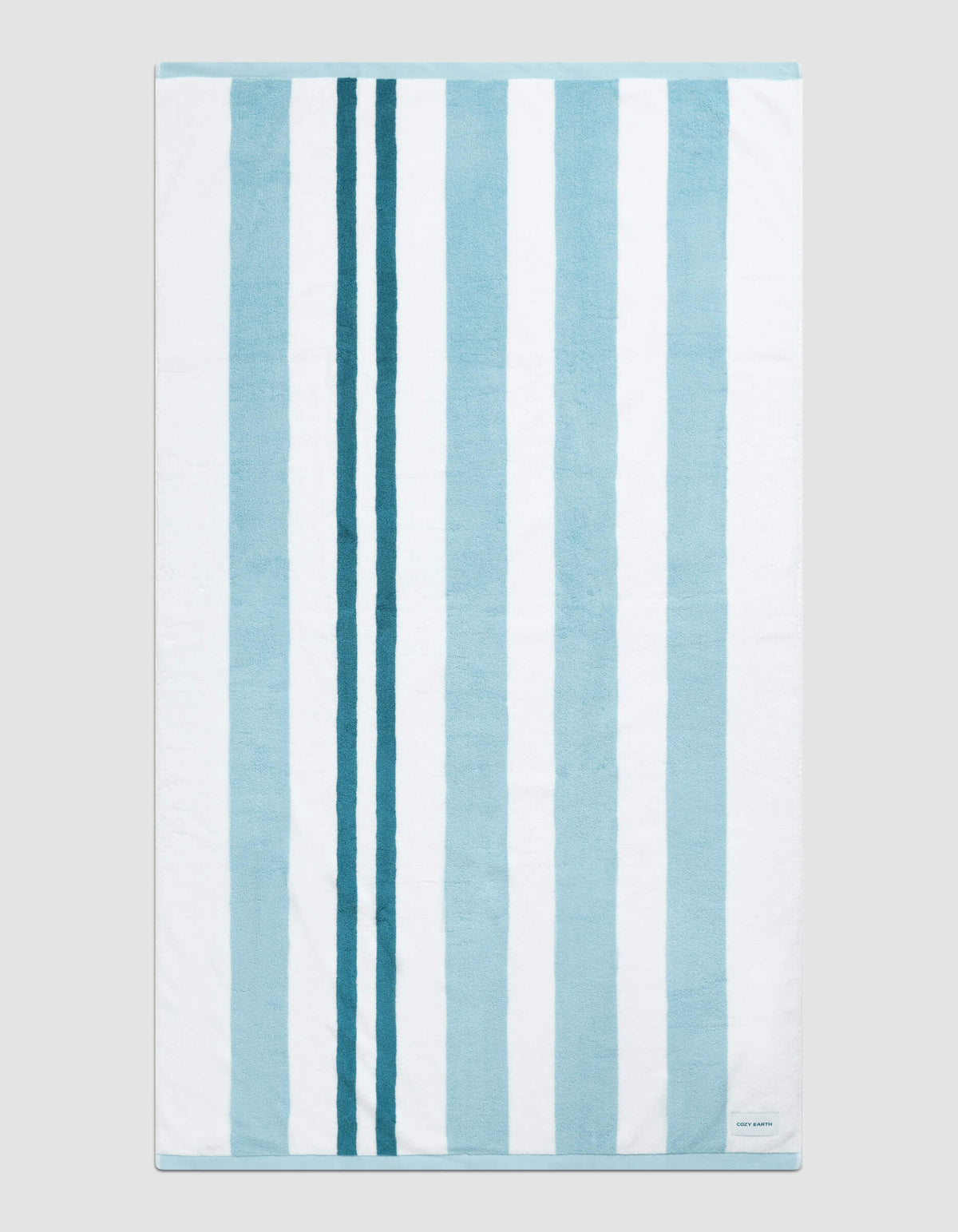 The Classic Stripe Resort Towel by Cozy Earth in Wave Stripe is shown laid flat on a light gray background. Alternating vertical blue and white stripes and a small white label in the bottom right corner are visible.|Color:Wave Stripe