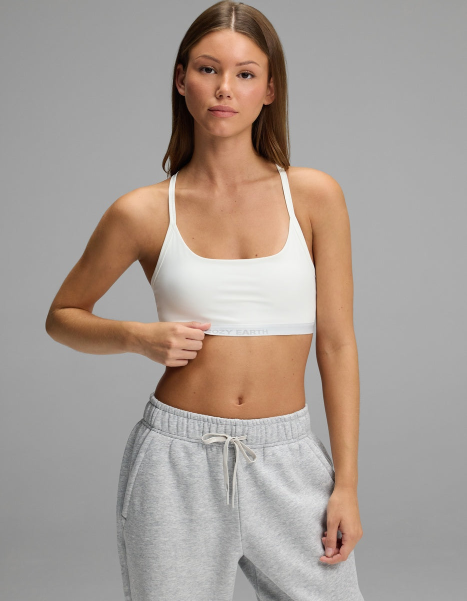 A woman wearing a white Cozy Earth Women’s Balance Bra with a branded elastic band and grey sweatpants.|Color:White