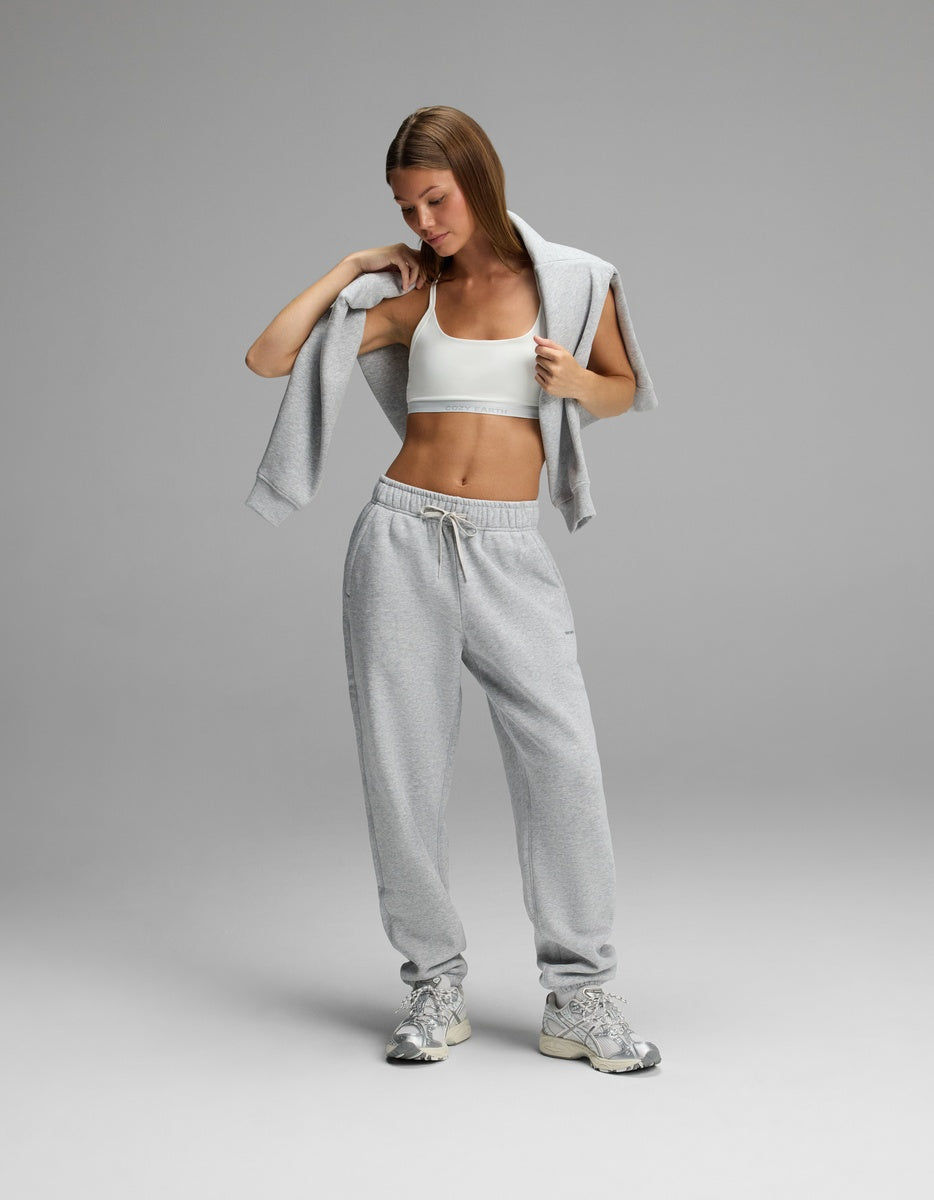 A person wearing a white Cozy Earth Women’s Balance Bra, gray sweatpants, and a gray sweatshirt draped over their shoulders.|Color:White