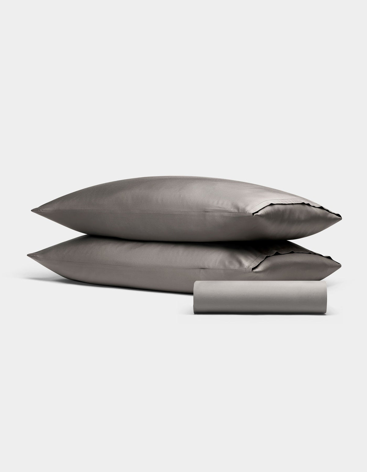The Bamboo Bedding Basic Bundle by Cozy Earth, featuring two gray pillows stacked and a folded gray bedsheet in front, is showcased against a plain white background.|Color:Charcoal