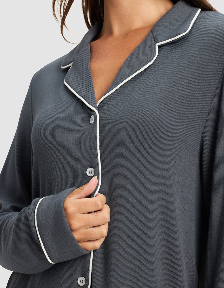 A woman wears the Cozy Earth Women's Bamboo Rib-Knit Classic Long Sleeve Pajama Top in dark gray with white piping, holding the front of the button-up shirt with her left hand.|Color:Graphite