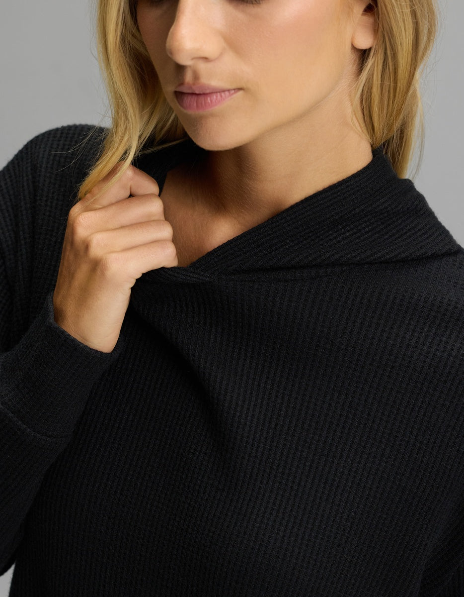 A person wearing a black Women’s Blake Waffle Hoodie, pulling the collar toward their neck.|Color:Jet Black