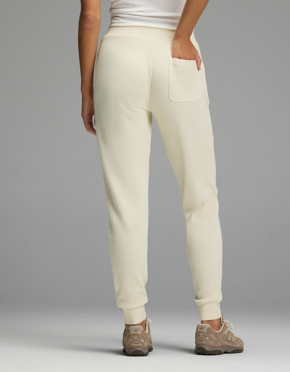Rear view of a person wearing cream-colored Women’s Blake Waffle Jogger pants with a back pocket and beige sneakers.|Color:Coconut