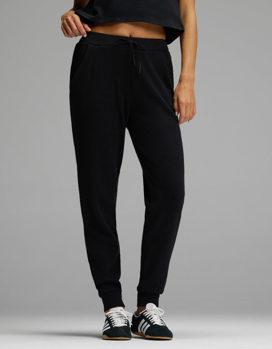 A person wearing black Women’s Blake Waffle Jogger pants with a drawstring waist and ribbed cuffs, paired with black and white sneakers.|Color:Jet Black