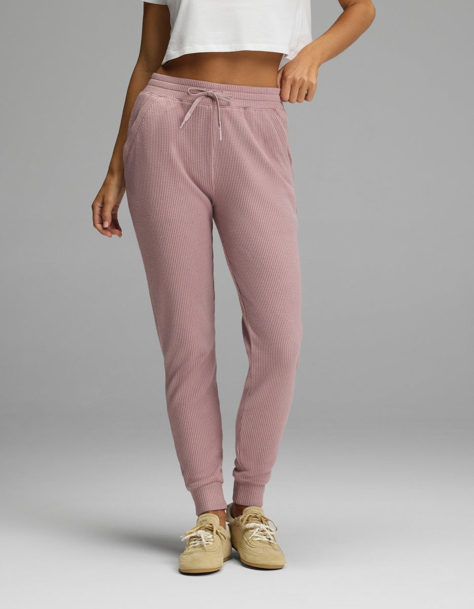 A person wearing mauve Women’s Blake Waffle Jogger pants with a drawstring waist and ribbed cuffs, paired with tan sneakers.|Color:Viola
