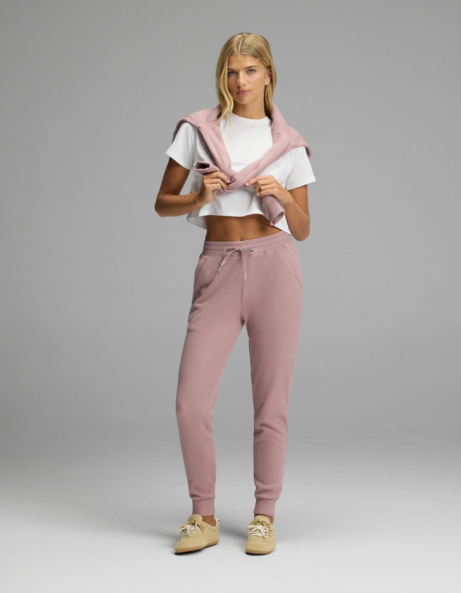 A person wearing a white t-shirt, a pink sweater draped over their shoulders, and pink textured Women’s Blake Waffle Jogger pants with a drawstring waist.|Color:Viola