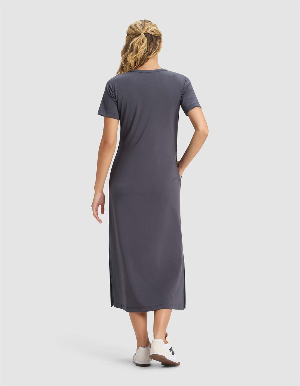 A woman with wavy blonde hair wears a Cozy Earth Women's Brushed Bamboo Midi Dress in gray and white shoes, standing with her back to the camera against a plain light background.|Color:Graphite