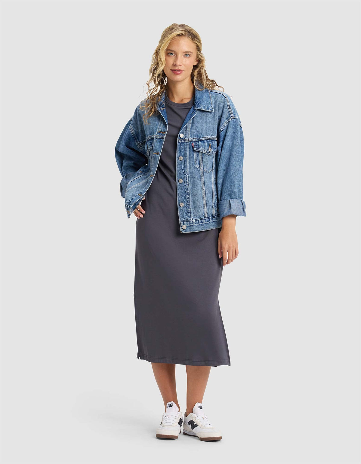A woman with wavy blonde hair and a confident expression wears the Cozy Earth Women's Brushed Bamboo Midi Dress in dark gray, styled with a blue denim jacket and white sneakers against a plain background.|Color:Graphite