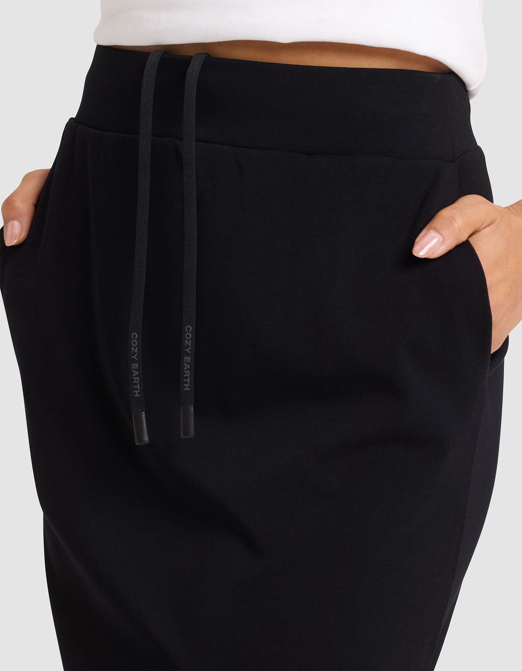 A person is shown from the waist down wearing the Cozy Earth Women's Brushed Bamboo Skirt in black, with hands in pockets, against a plain background. |Color:Black
