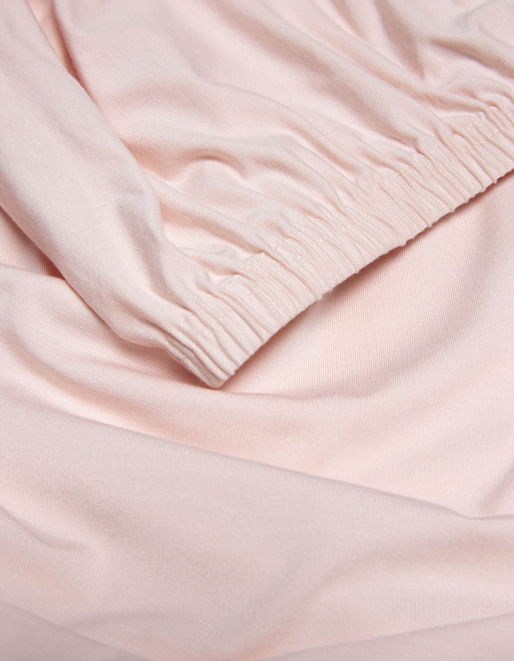 Close-up of Cozy Earth’s Bamboo Jersey Fitted Sheet in light pink, highlighting its smooth texture, soft folds, and gathered elastic cuff detail.|Color:Petal
