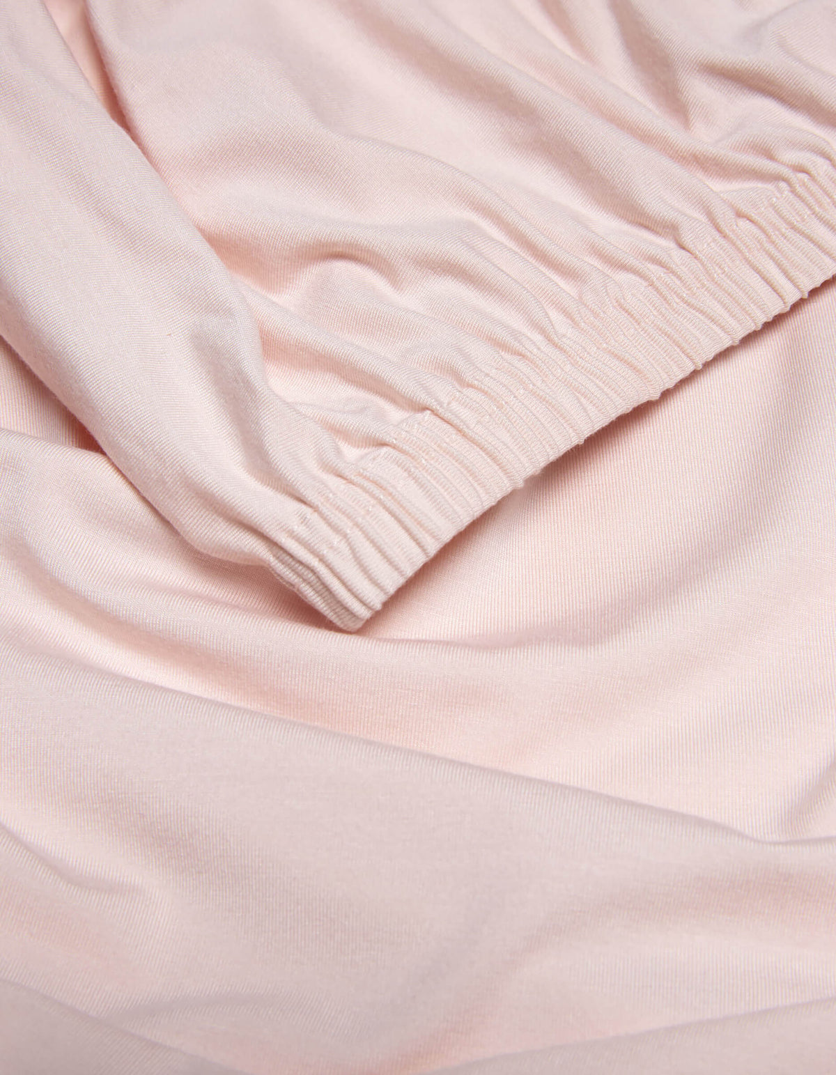 Close-up of Cozy Earth’s Bamboo Jersey Fitted Sheet in light pink, highlighting its smooth texture, soft folds, and gathered elastic cuff detail.|Color:Petal