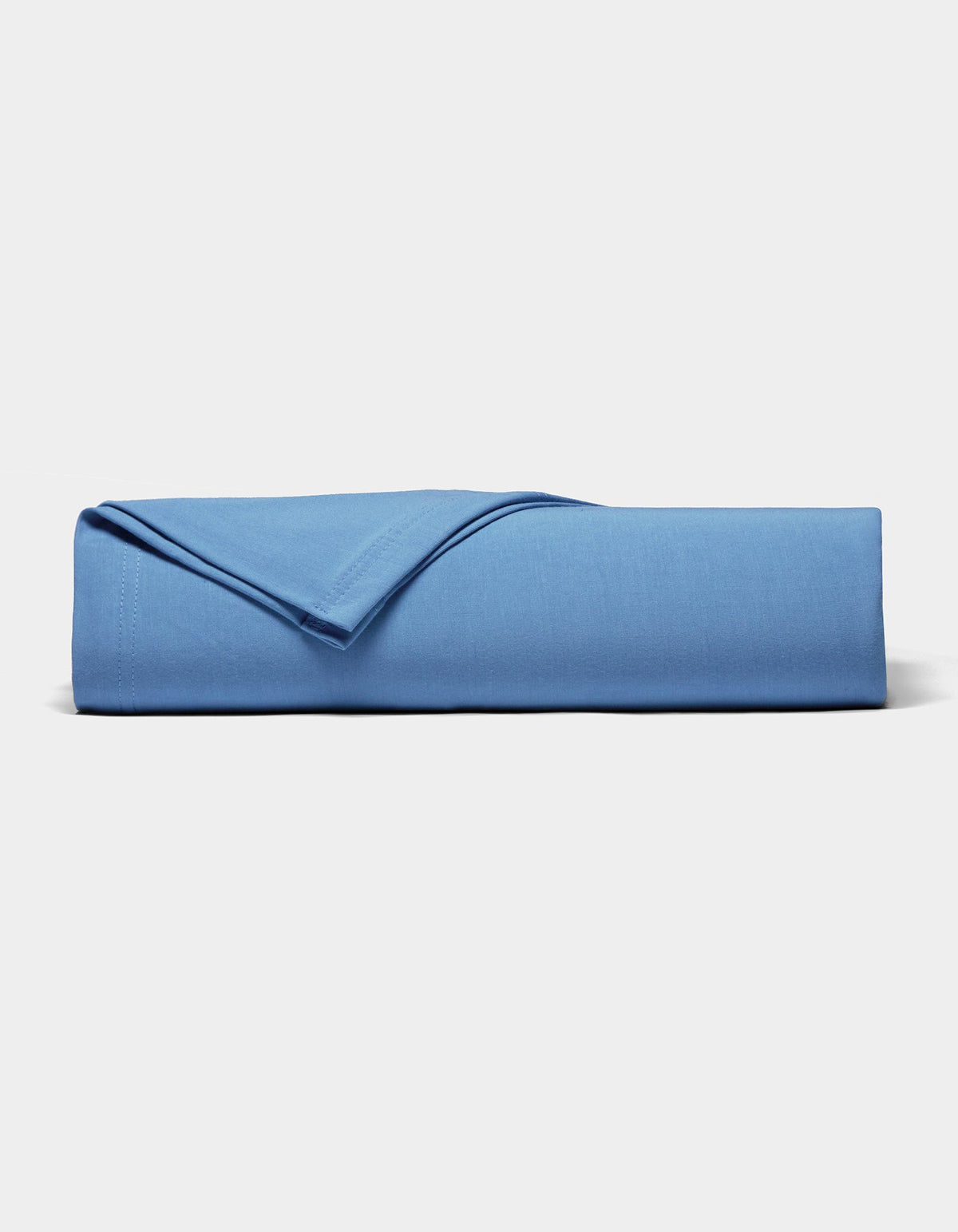 A neatly folded Bamboo Jersey Sheet Set by Cozy Earth in blue rests on a plain white surface, with one corner flipped to display the soft fabric texture.|Color:Sailor