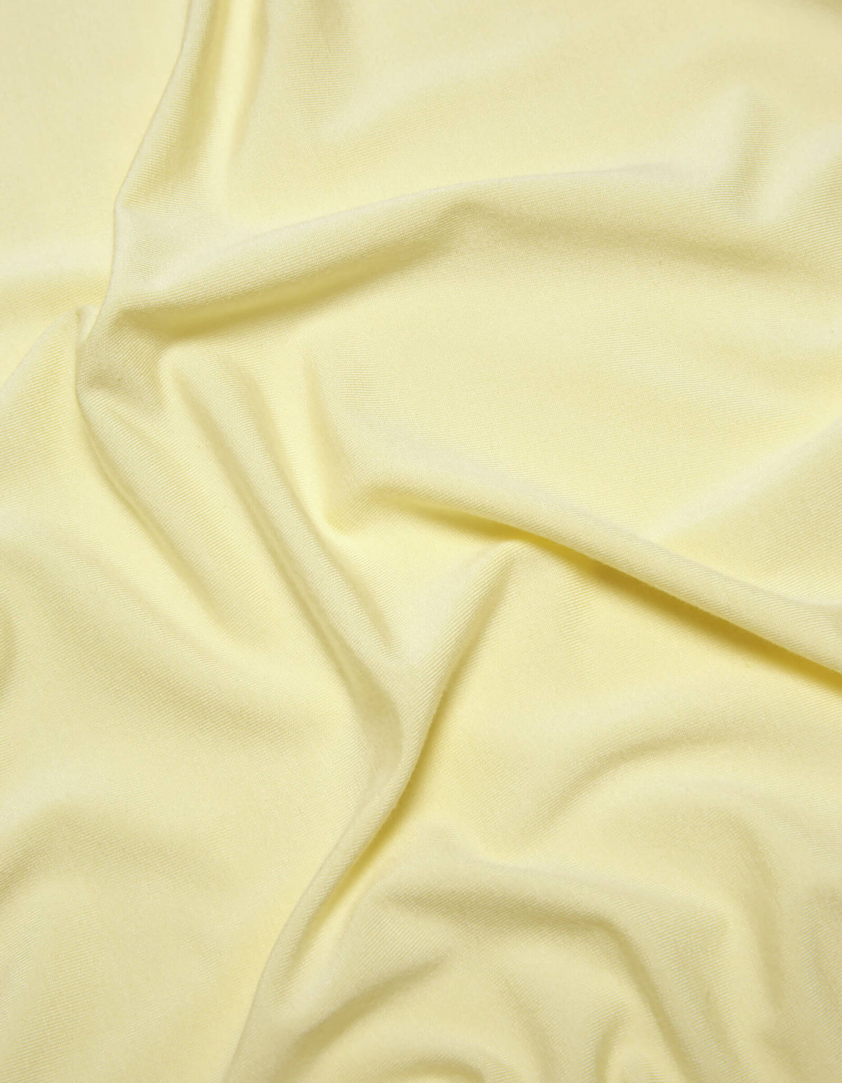 A close-up of Cozy Earth's Bamboo Jersey Sheet Set in pale yellow, featuring soft folds and gentle wrinkles for a smooth, slightly textured look.|Color:Meringue