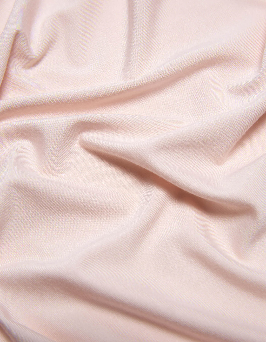 The Bamboo Jersey Sheet Set by Cozy Earth features soft, light pink fabric with subtle folds and gentle wrinkles for a smooth, slightly textured look.|Color:Petal