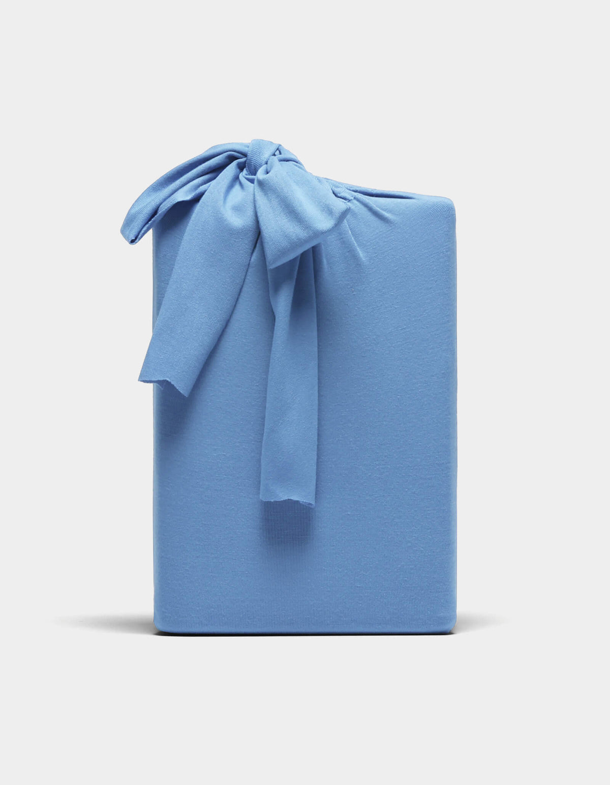 A Bamboo Jersey Sheet Set by Cozy Earth, neatly folded and wrapped in light blue fabric with a matching bow, displayed against a plain white background.|Color:Sailor