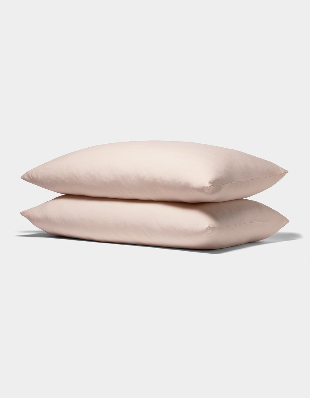 Two Bamboo Jersey Pillowcases from Cozy Earth, in soft light pink, are stacked neatly against a plain white background.|Color:Petal