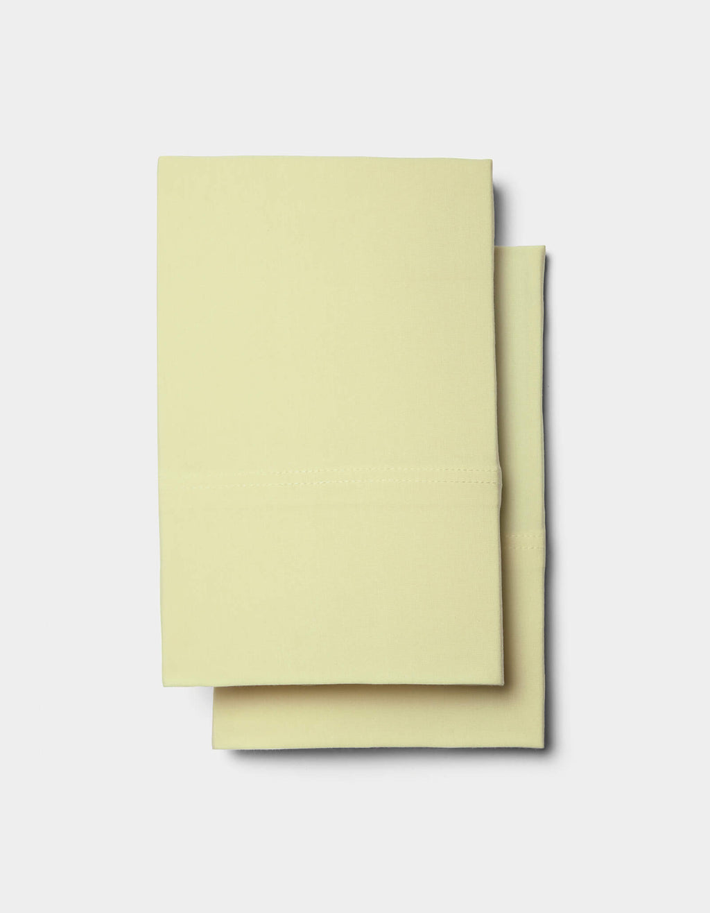 Two neatly folded Bamboo Jersey Sheet Sets by Cozy Earth in pale yellow are stacked on a plain white background.|Color:Meringue