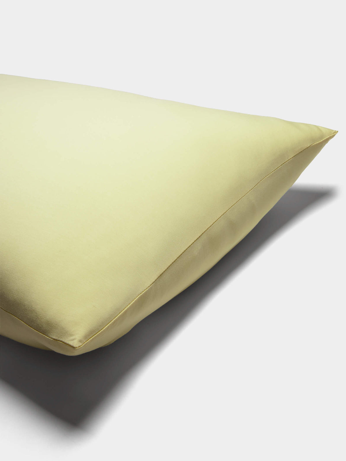 A close-up of a pale yellow Cozy Earth Bamboo Jersey Pillowcase with a smooth surface, set on a white background and casting a soft shadow to the right.|Color:Meringue