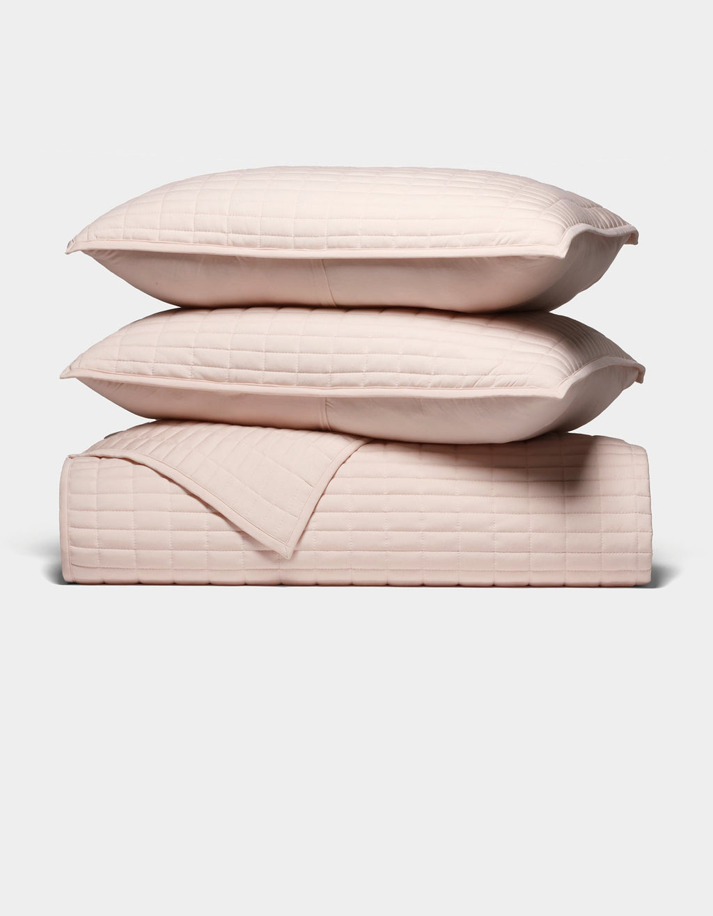 The Cozy Earth Bamboo Jersey Quilt Bundle features two light pink quilted pillows stacked atop a matching quilted blanket, all neatly arranged against a plain white background.|Color:Petal