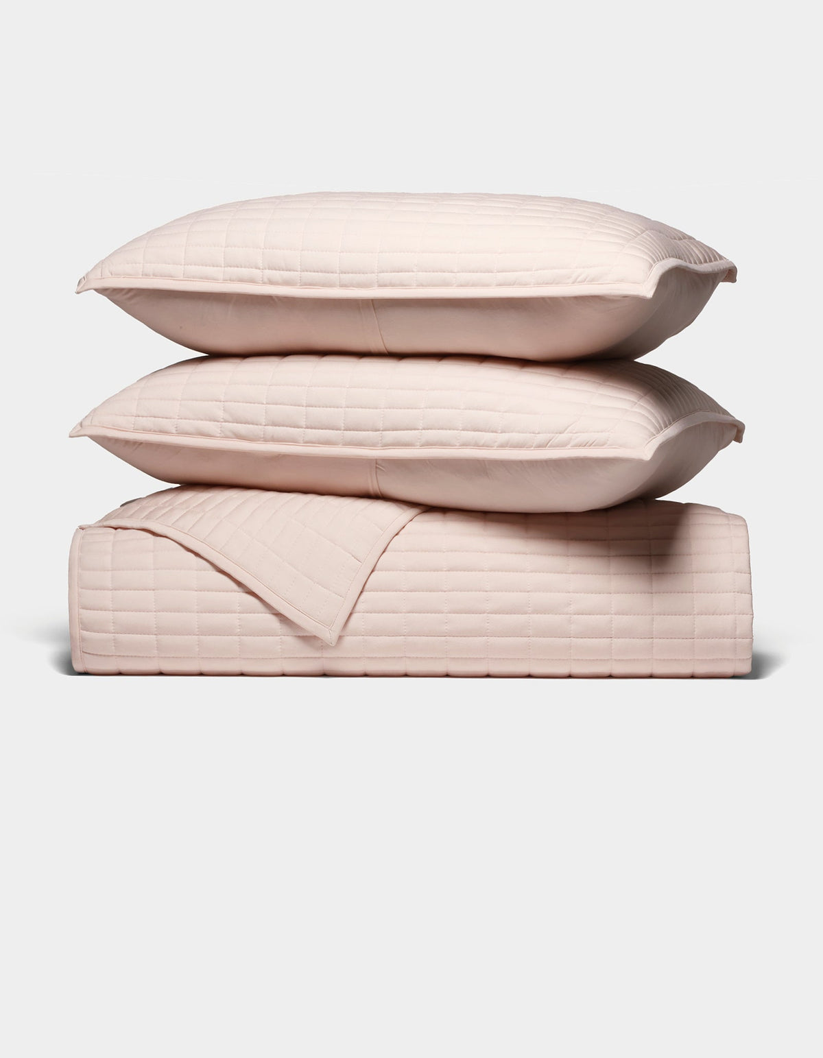 The Cozy Earth Bamboo Jersey Quilt Bundle features two light pink quilted pillows stacked atop a matching quilted blanket, all neatly arranged against a plain white background.|Color:Petal