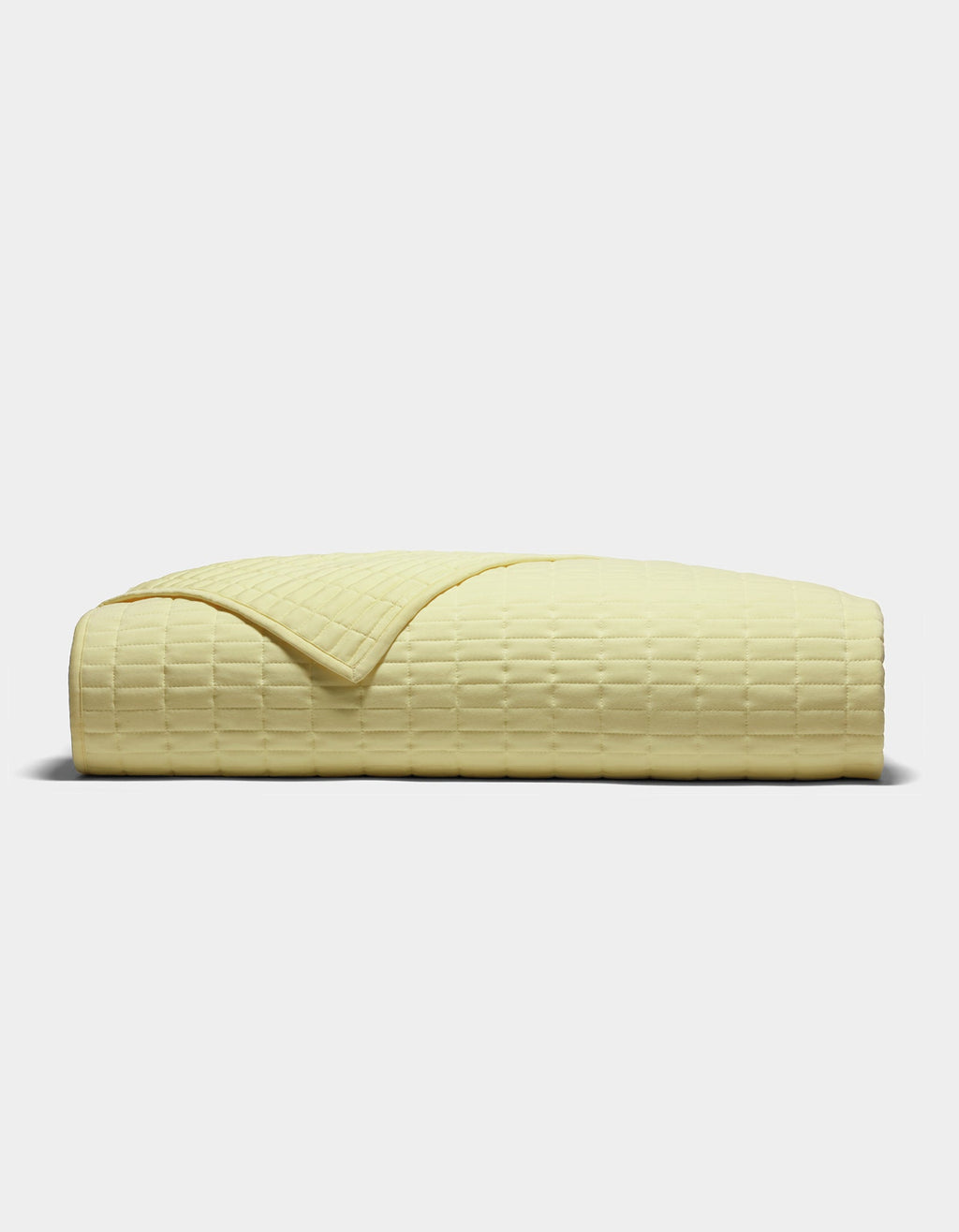 The Cozy Earth Bamboo Jersey Quilt, shown folded from the side on a plain light background, features a pale yellow color and a subtle grid-like textured pattern.|Color:Meringue