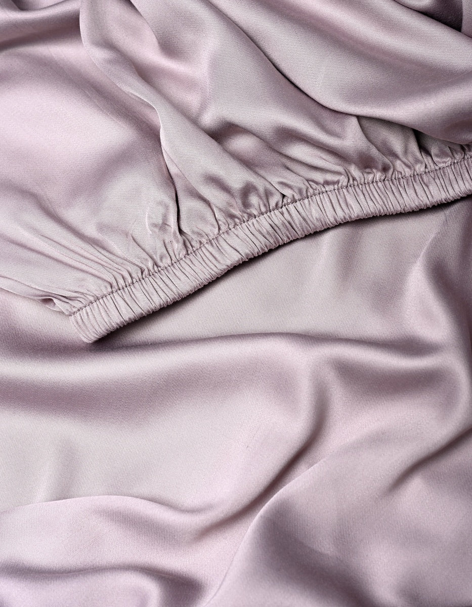Close-up of soft, light lavender Bamboo Fitted Sheet by Cozy Earth, featuring a gathered, ruched elastic seam at the top and smooth, flowing folds below.|Color:Lavender