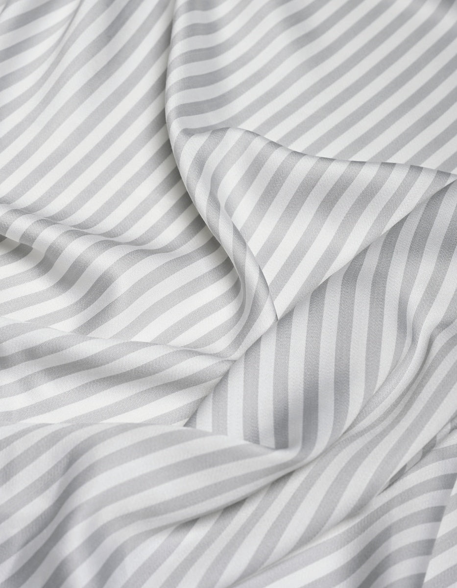The Cozy Earth Bamboo Flat Sheet features a white fabric with diagonal light gray stripes that drape softly, forming gentle folds and shadows. The consistent pattern and smooth, silky texture enhance its luxurious feel.|Color:Classic Stripe in Dew
