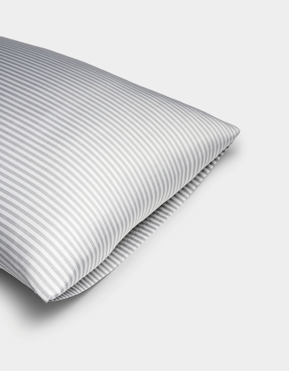 A close-up of a Bamboo Pillowcase by Cozy Earth, featuring gray and white vertical stripes, set against a plain white background.|Color:Classic Stripe in Dew