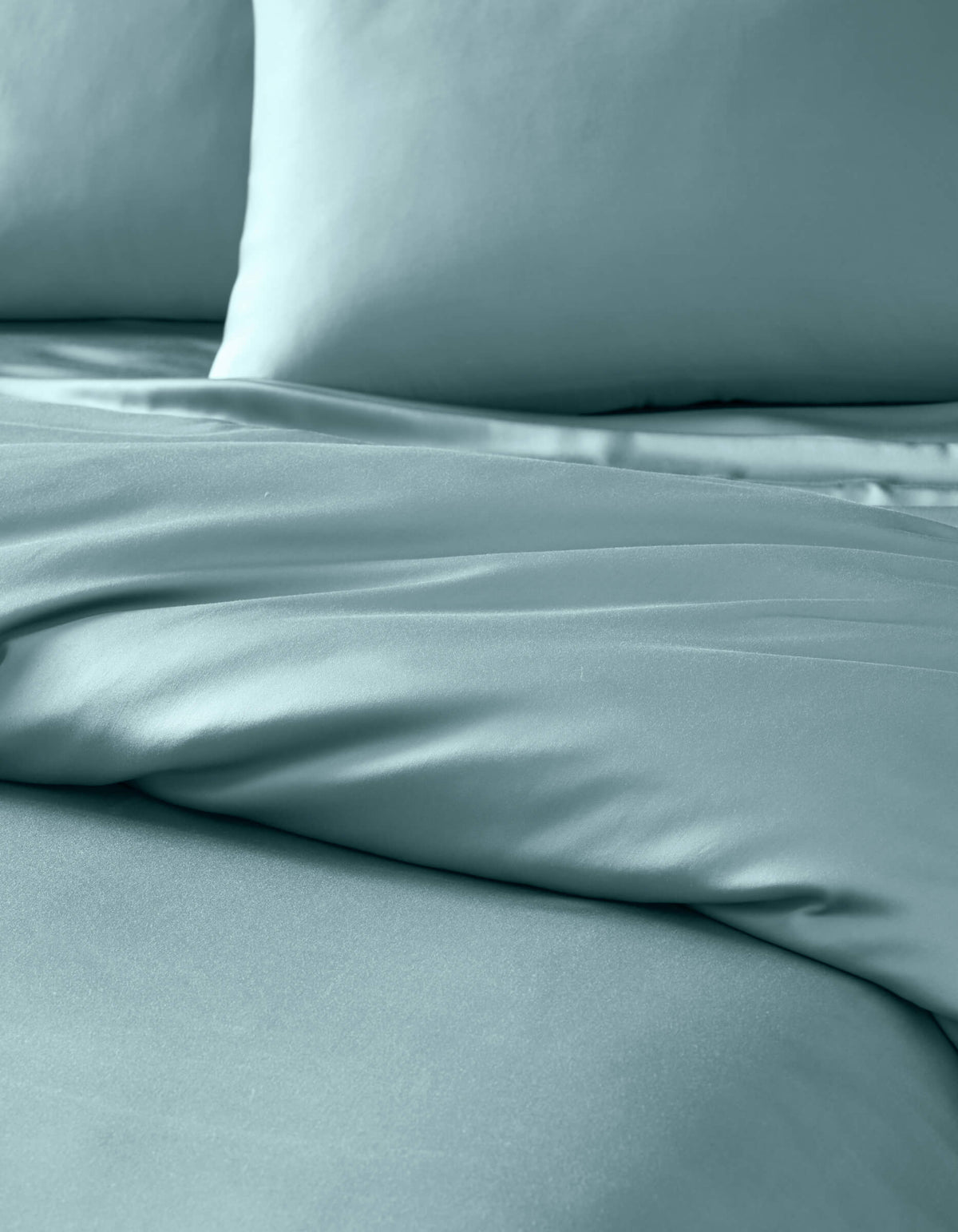 Close-up of a neatly made bed featuring the Cozy Earth Bamboo Duvet Cover in light blue, with two matching pillows. The smooth, soft fabric displays gentle folds for a luxurious look.|Color:River