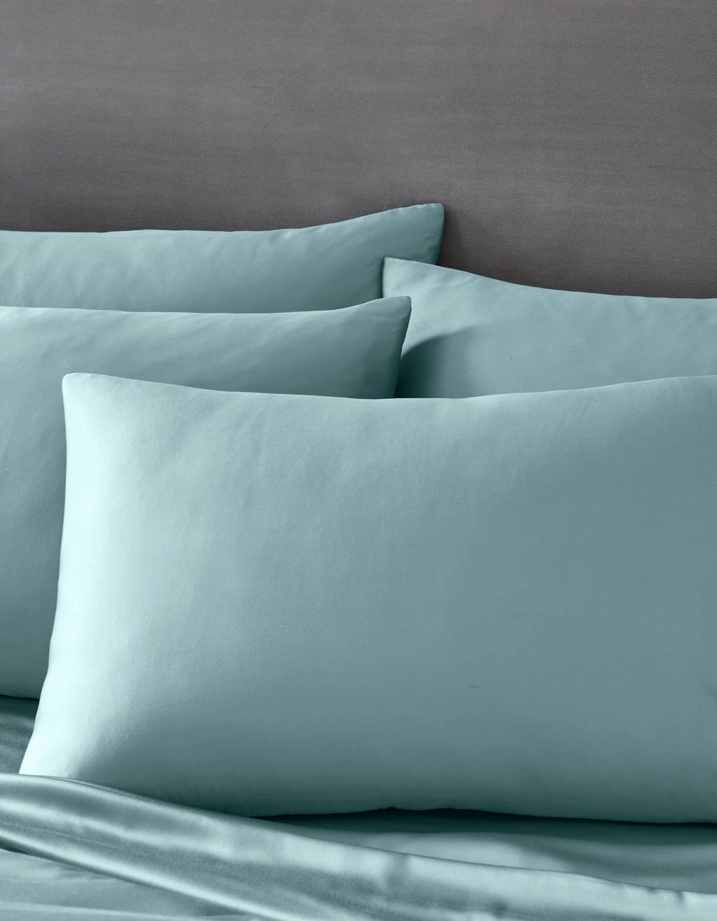 Cozy Earth's Bamboo Pillowcases in light blue are paired with matching bedsheets on a bed with a gray headboard, creating a calm and inviting atmosphere.|Color:River