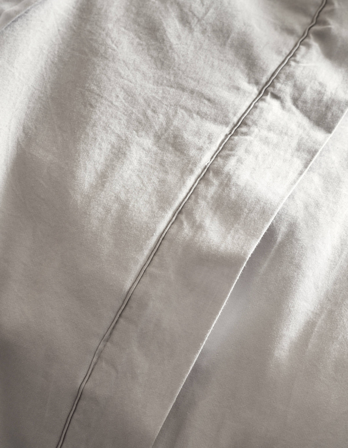 Close-up of Cozy Earth’s Soft-Wash Cotton Quilt in light gray, featuring a prominent vertical stitched seam, gentle folds, and a smooth, soft texture.|Color:Dew
