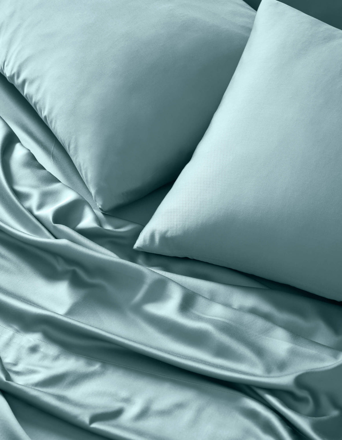 A close-up of Cozy Earth's Bamboo Sheet Set in light blue, neatly arranged with two matching pillows. The smooth, soft fabric shows subtle folds and a gentle sheen for an inviting look.|Color:River