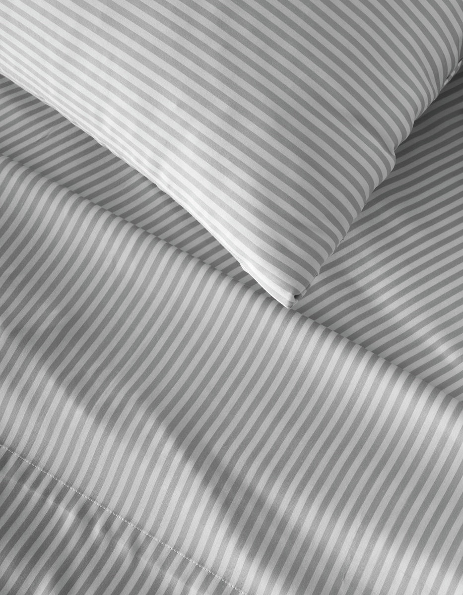 Close-up of a bed with a pillow and sheets featuring the Bamboo Flat Sheet from Cozy Earth in a gray and white diagonal stripe pattern.|Color:Classic Stripe in Dew