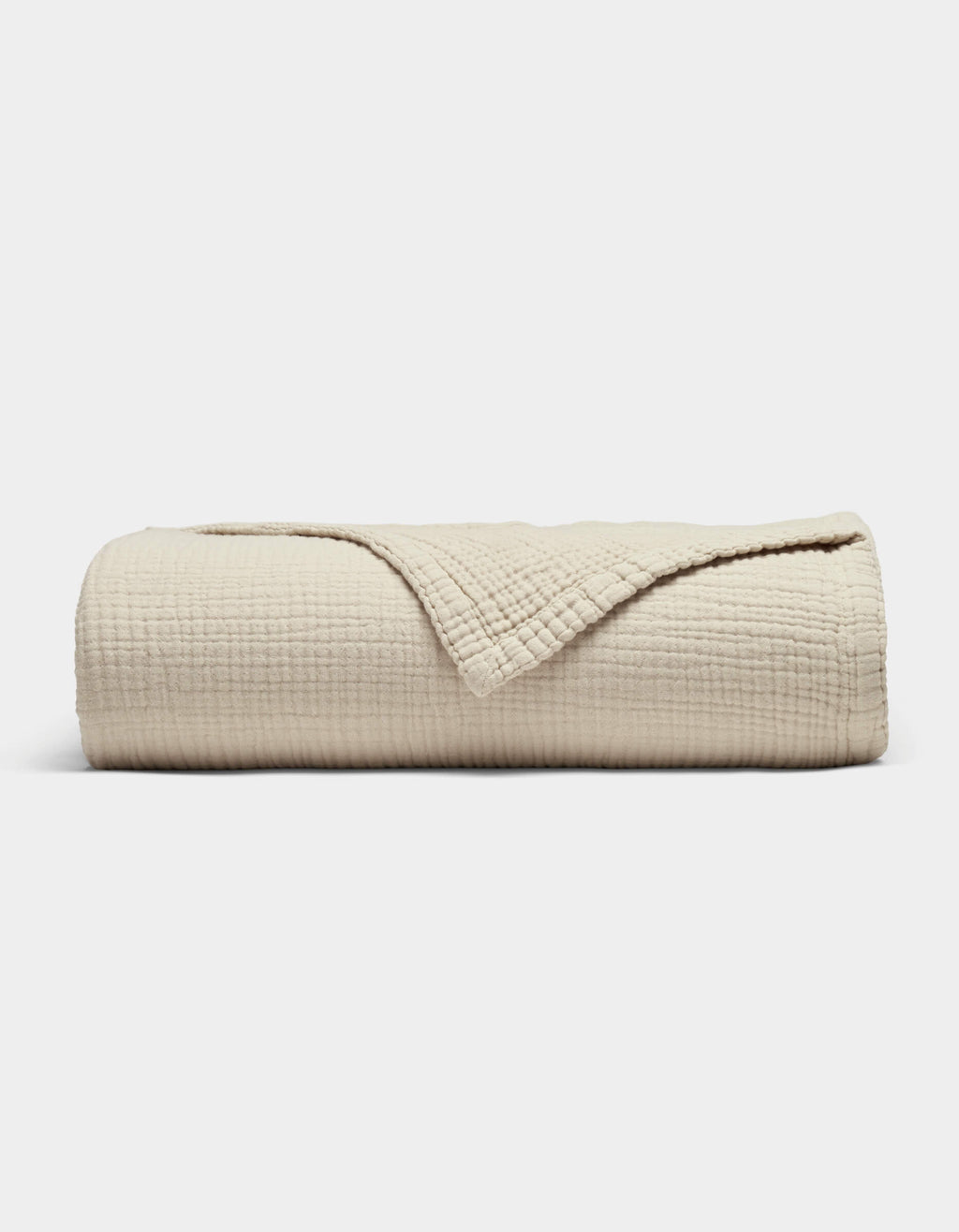 The Cozy Earth Cotton Gauze Blanket, in beige with a soft grid texture, is neatly rolled with a corner folded back to reveal its fabric, shown against a plain white background.|Color:Coconut