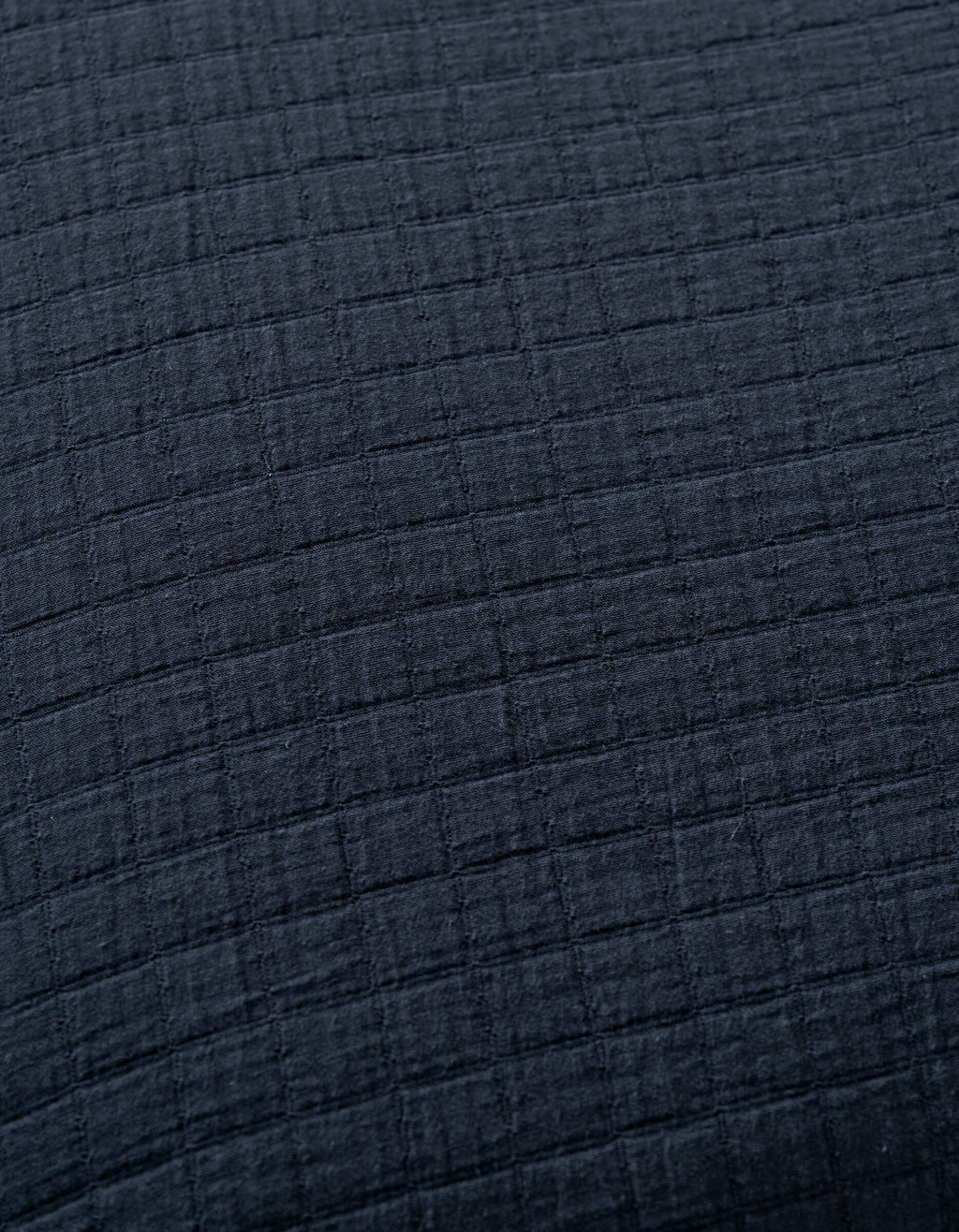 Close-up of Cozy Earth's Waterfront Grid Matelasse Blanket in dark gray or black, featuring a soft textured fabric with a subtle grid pattern formed by raised horizontal and vertical lines.|Color:Eclipse