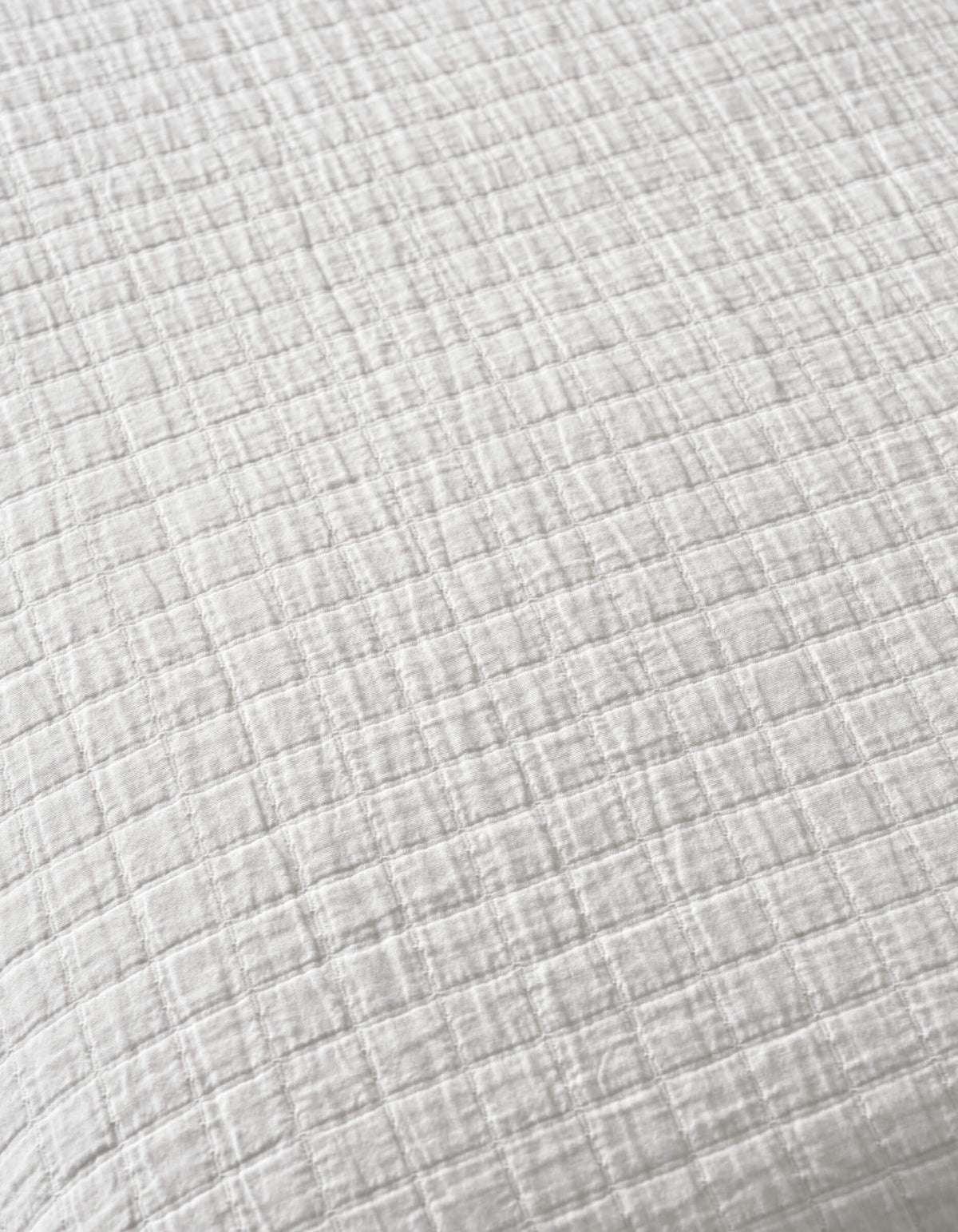 A close-up of Cozy Earth's Waterfront Grid Matelasse Blanket, featuring white fabric with a subtle checkered texture, small raised squares, and soft, crinkled material.|Color:Sea Salt