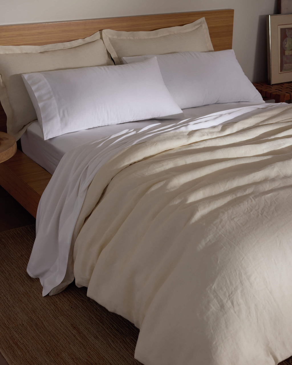 A bed features the Cozy Earth Linen Duvet Cover, white pillows, and a wooden headboard. A bedside table adds warmth to the softly lit room, creating a cozy and inviting atmosphere.|Color:Flax